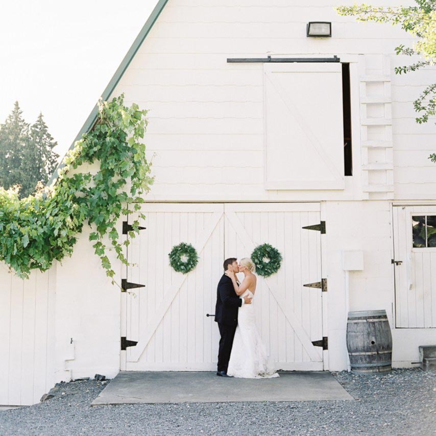 Bride and groom kissing in front of white barn | Lisa Dupar Catering | Wedding & Event Catering in Seattle